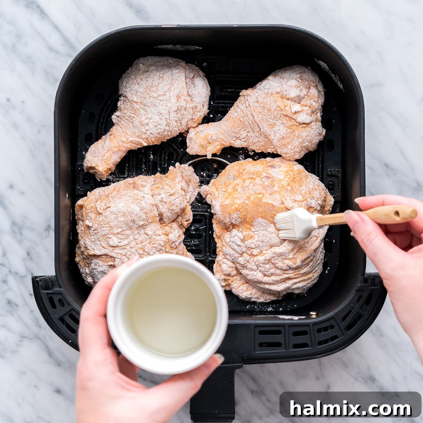 A close-up of a breaded chicken piece in the air fryer basket, being generously brushed with vegetable oil just before cooking to ensure a rich, golden, and crispy finish.