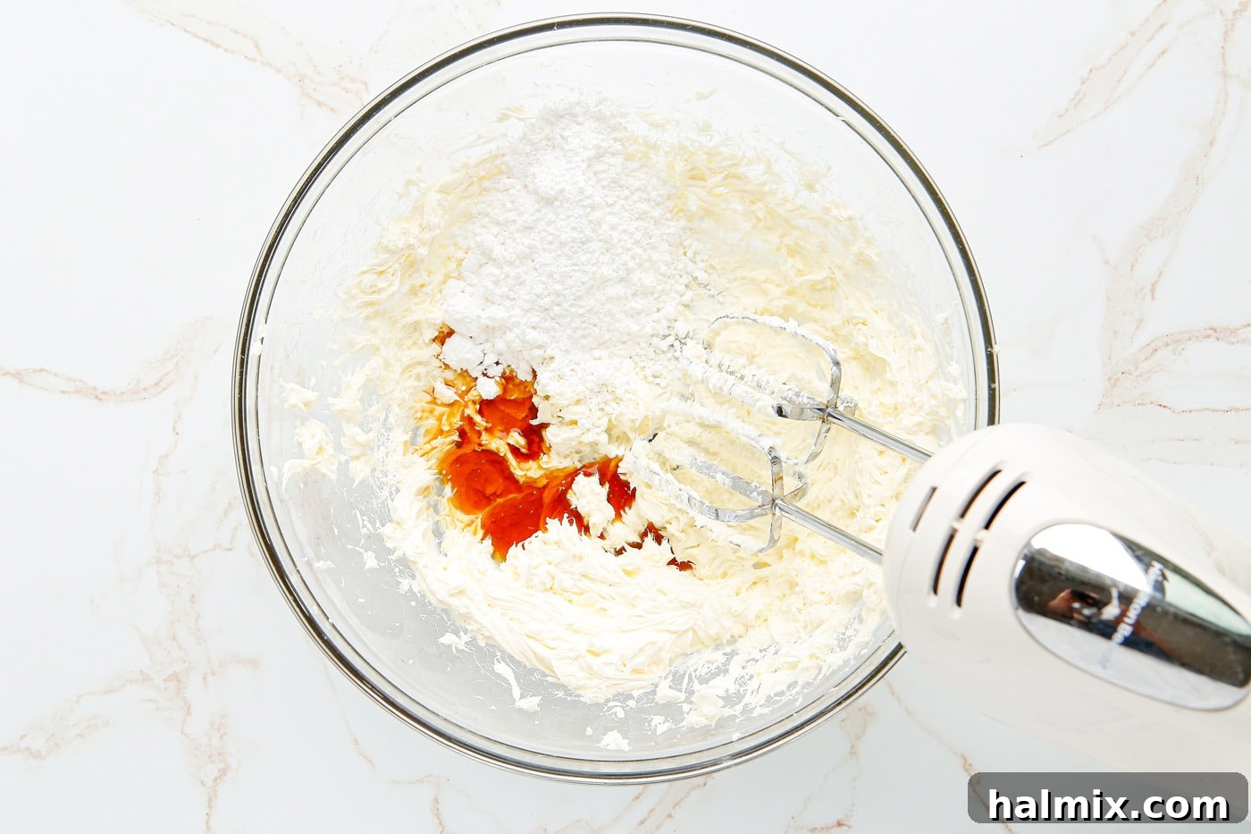 Adding powdered sugar, heavy cream, and vanilla extract to the beaten cream cheese mixture.