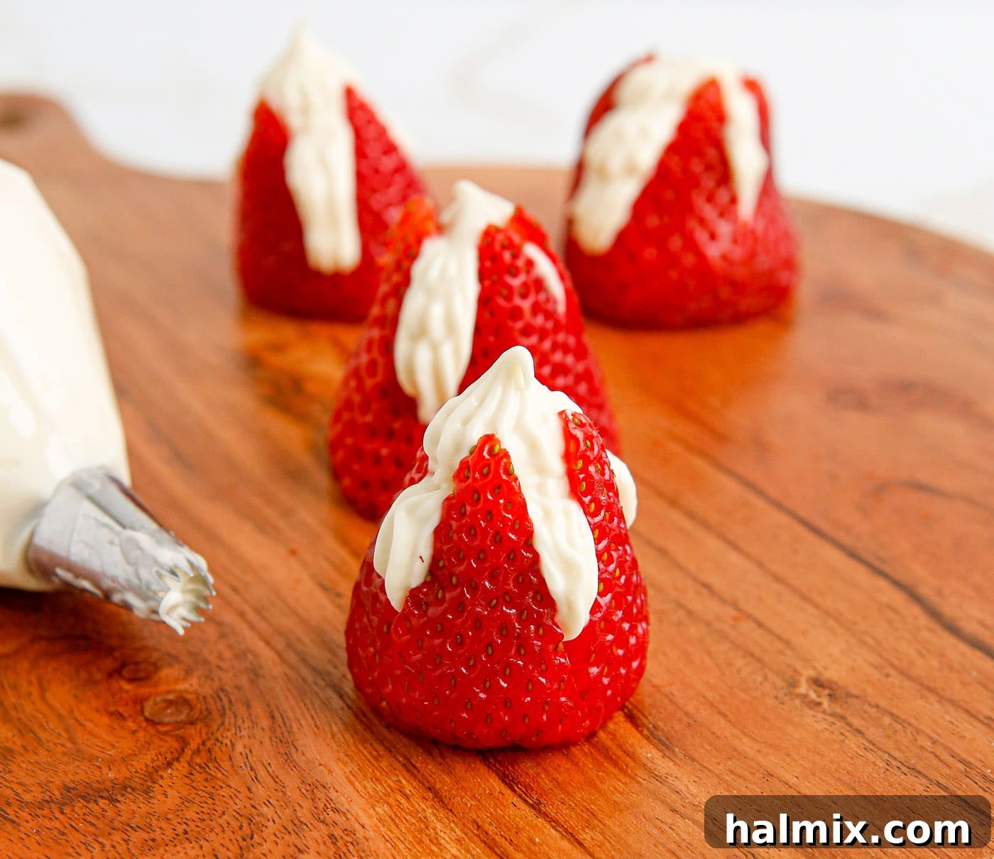 Piping creamy cheesecake filling into the prepared strawberries using a pastry bag.