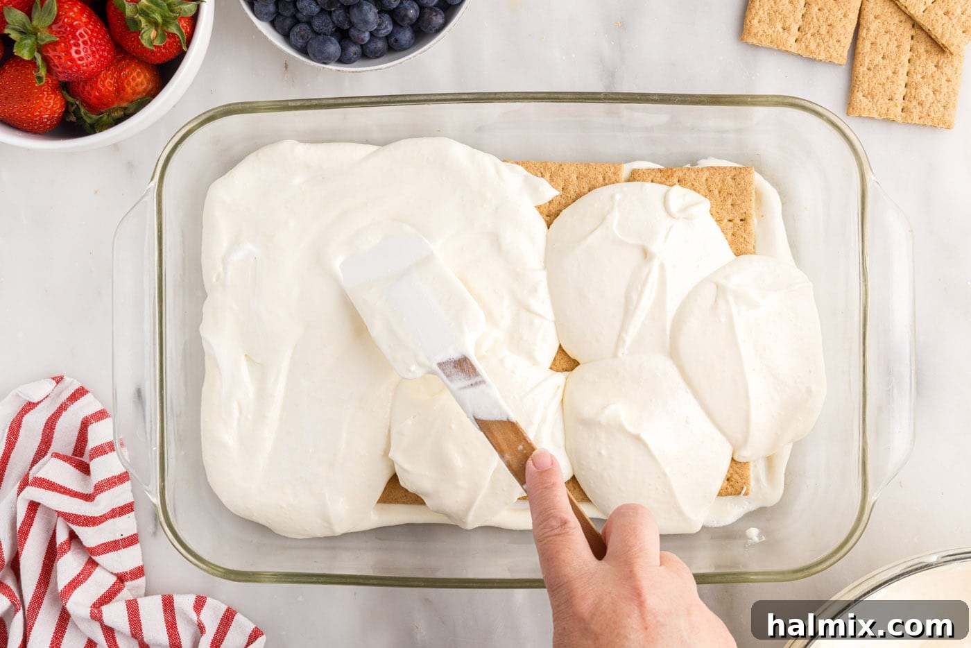 Spreading a thin layer of pudding mixture over the graham crackers in the baking dish.