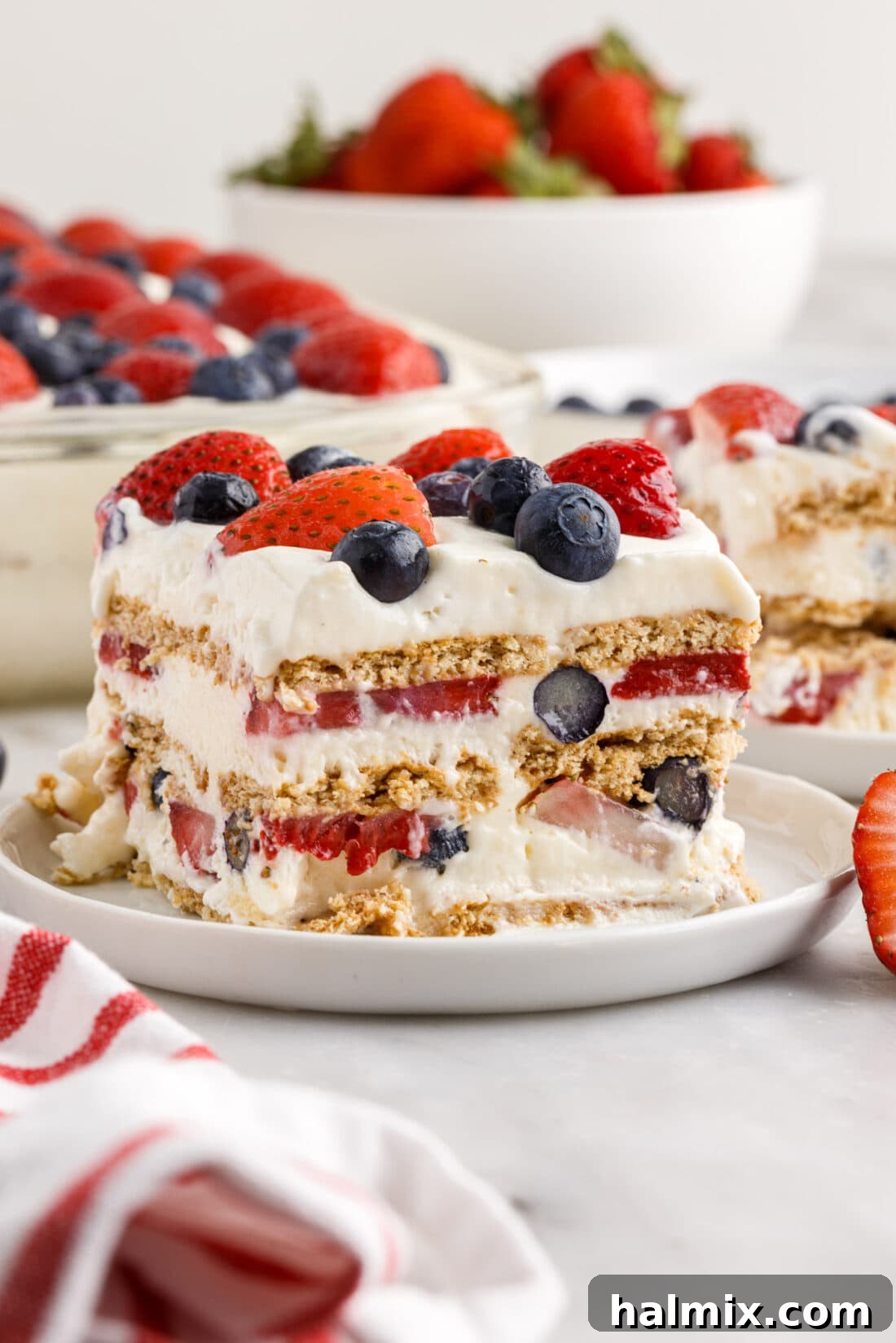 A perfectly sliced piece of Mixed Berry Icebox Cake served on a white plate, highlighting its distinct layers of creamy filling, graham crackers, and fresh berries.