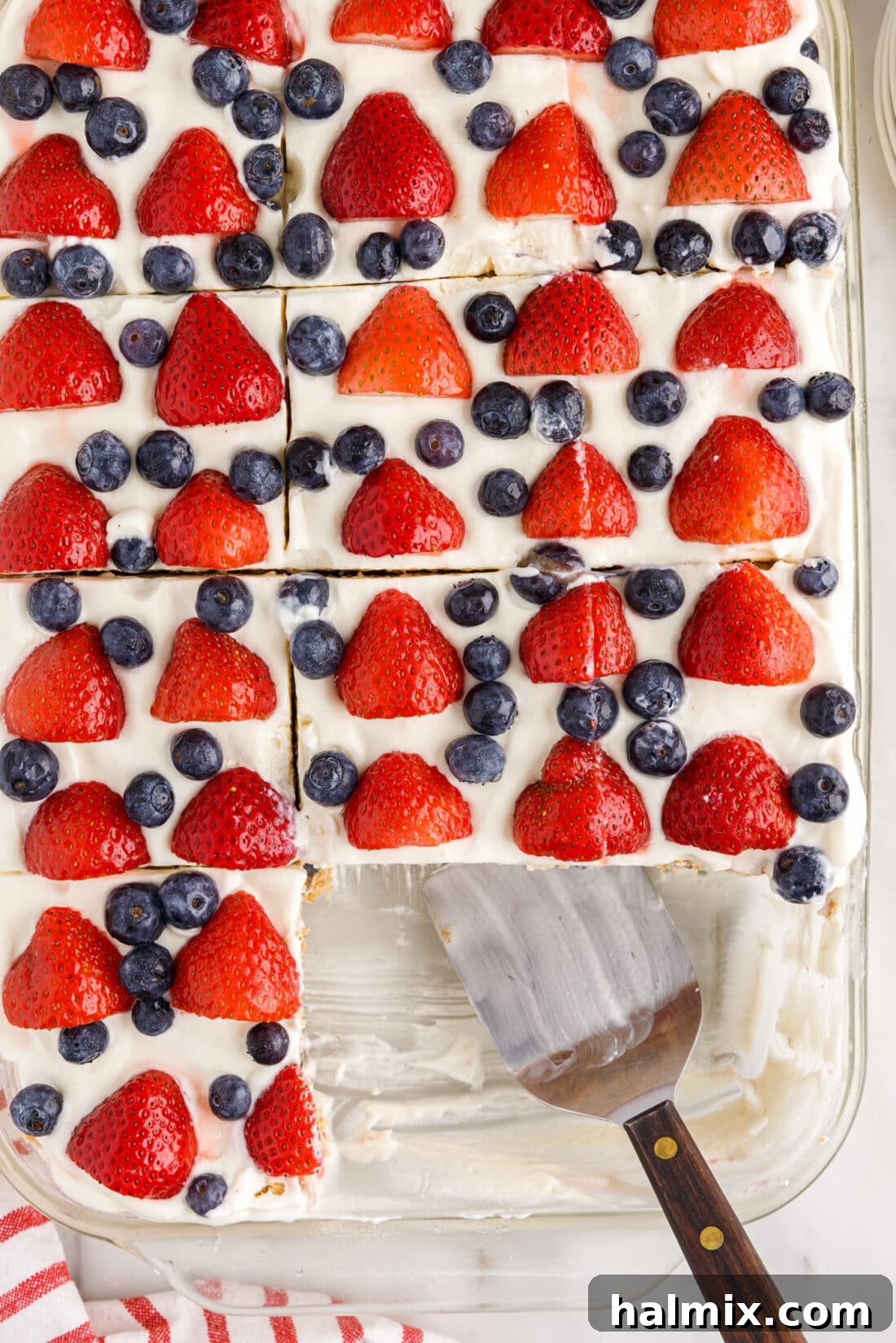 An overhead view of a Mixed Berry Icebox Cake with several slices already removed, revealing the beautiful layers, with a serving spatula in the pan.