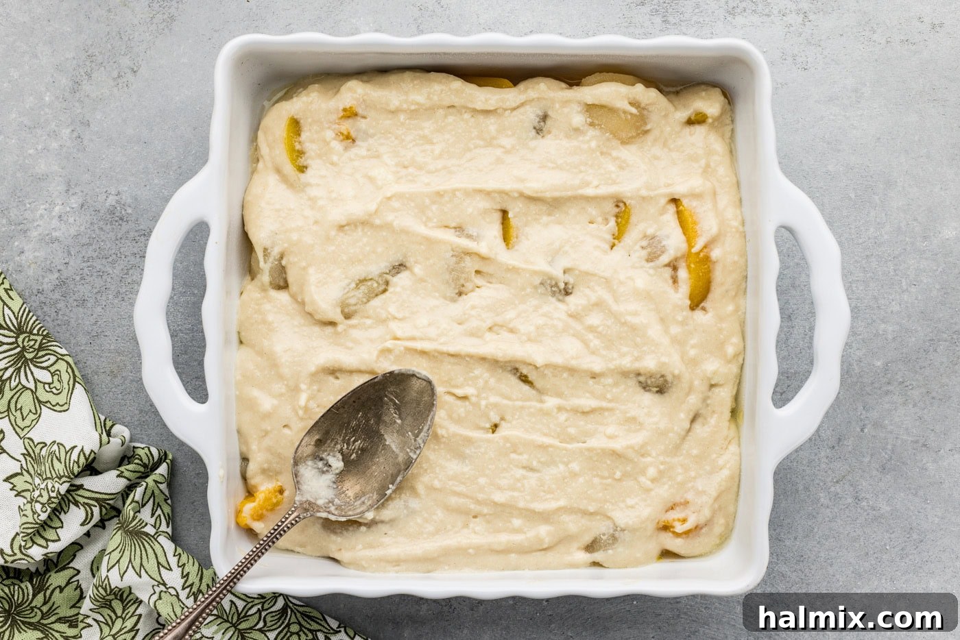 spoon spreading out cobbler batter on top of peaches and pears in a baking dish