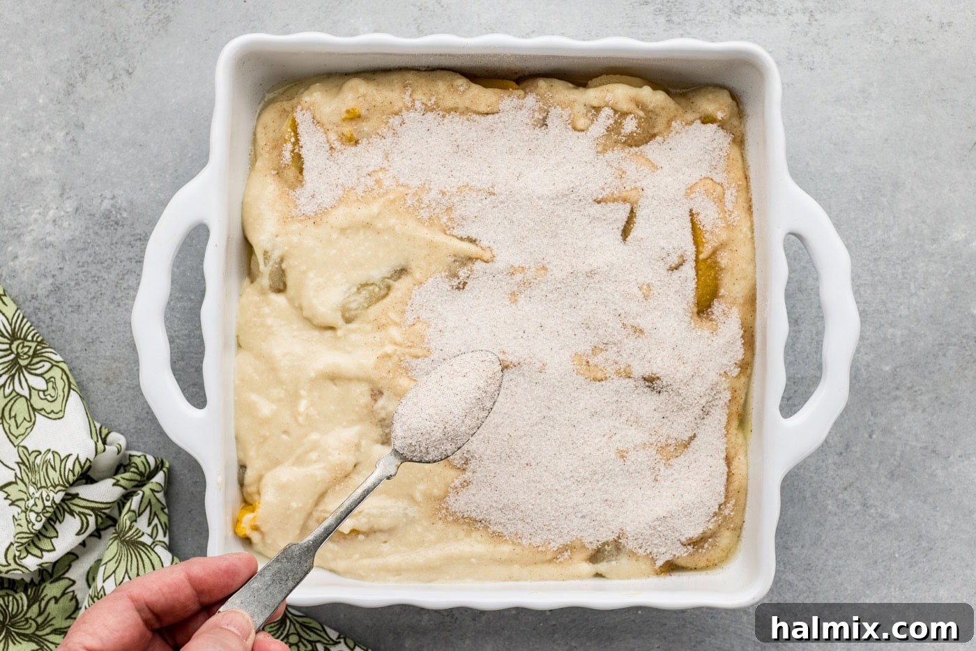 spoon sprinkling on sugar mixture over cobble batter in a dish