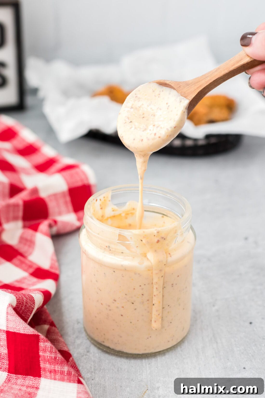 Spoon dripping Alabama White Sauce into a jar, highlighting its creamy texture.