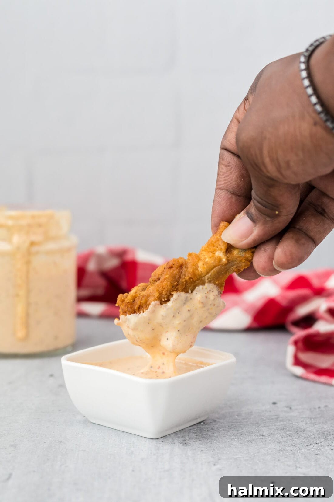 Dipping a crispy chicken wing into a bowl of creamy Alabama White Sauce.