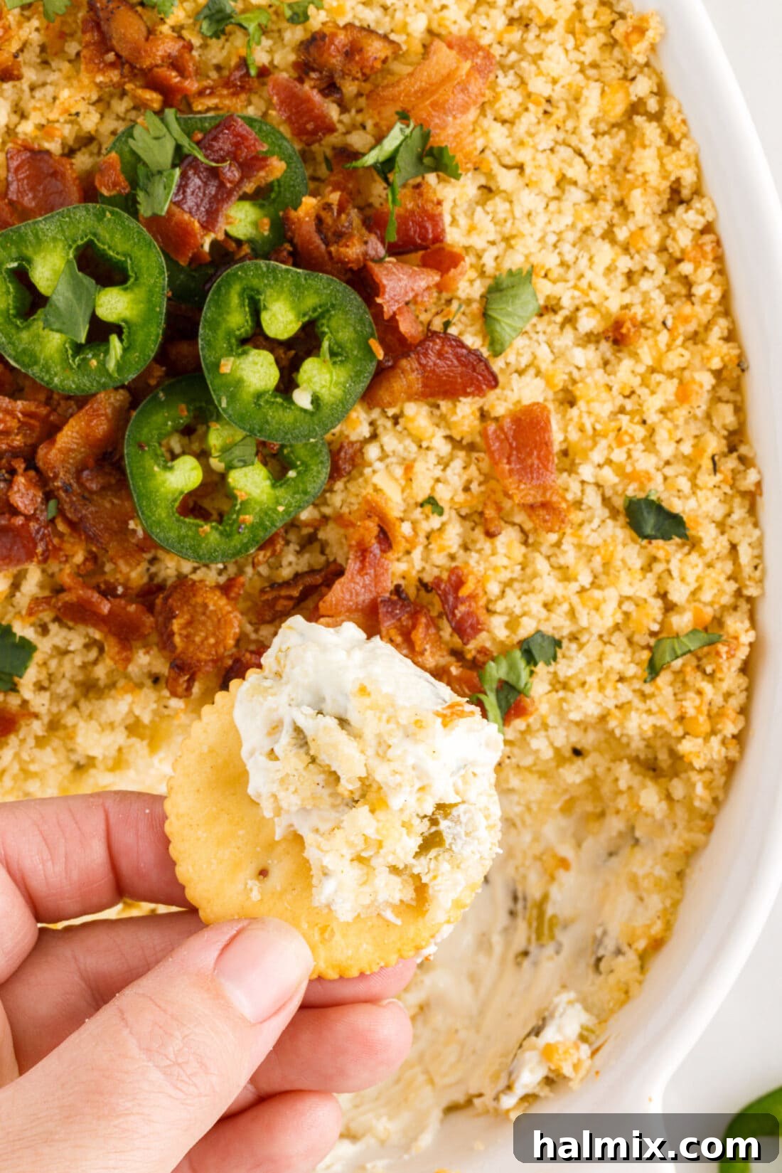 Hand lifting chip from a bubbling Jalapeno Popper Dip with a golden crust