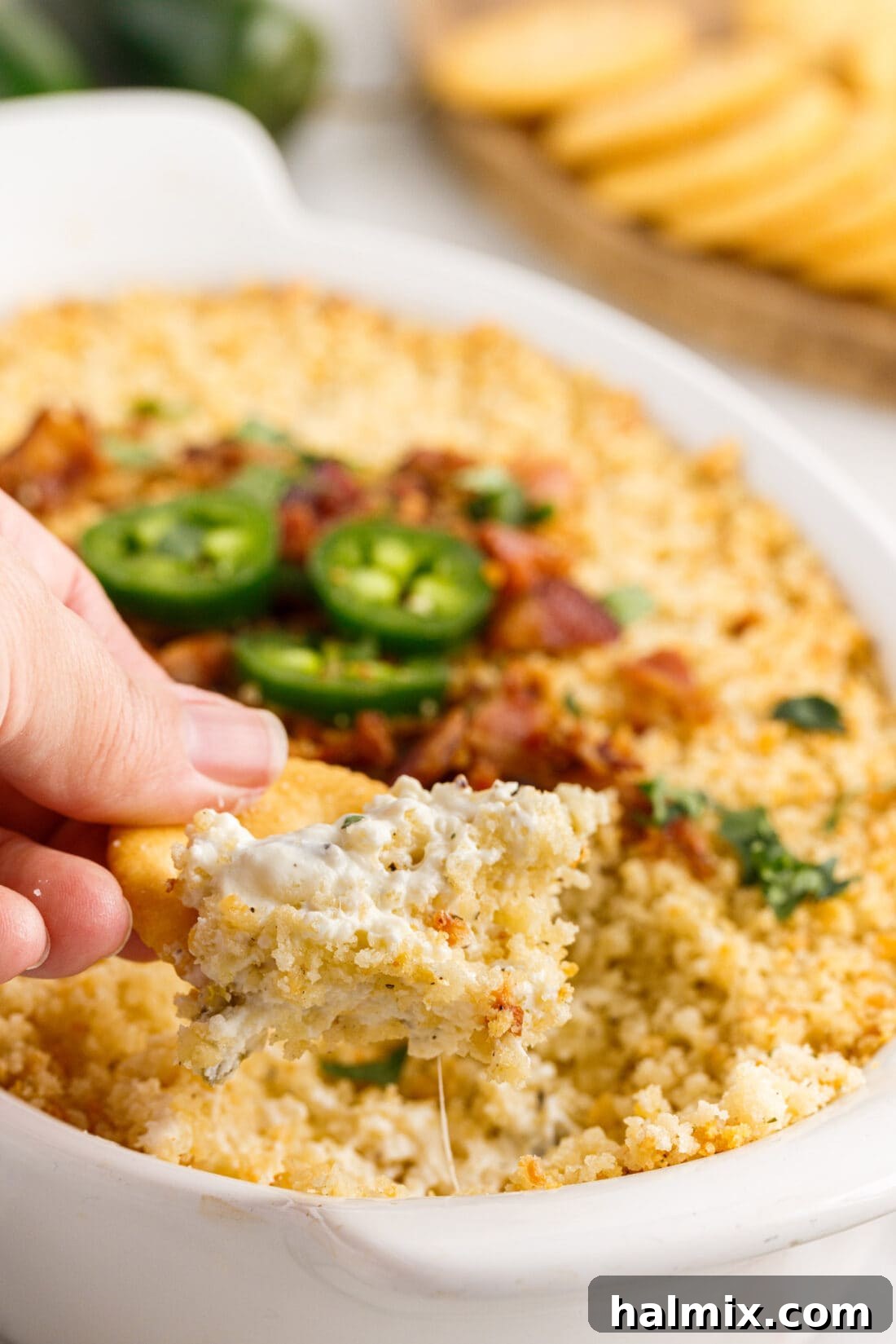 Cracker scooping a portion of creamy and cheesy Jalapeno Popper Dip from the dish
