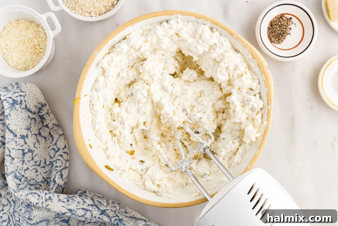A hand mixer blending the ingredients for jalapeno popper dip in a mixing bowl