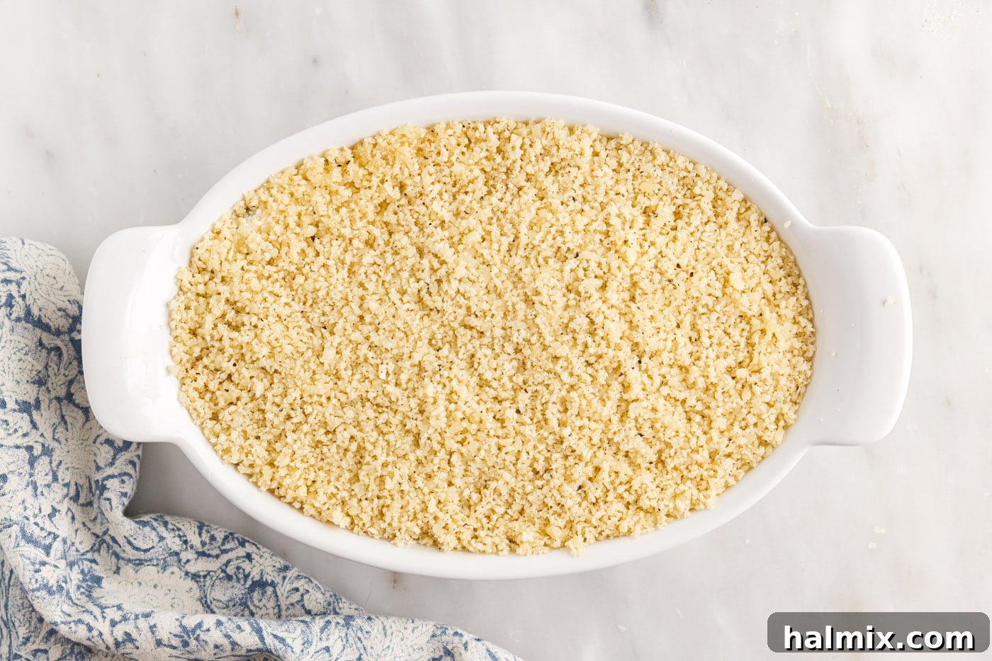 Buttered panko breadcrumbs being sprinkled evenly over the jalapeno popper dip mixture in a baking dish