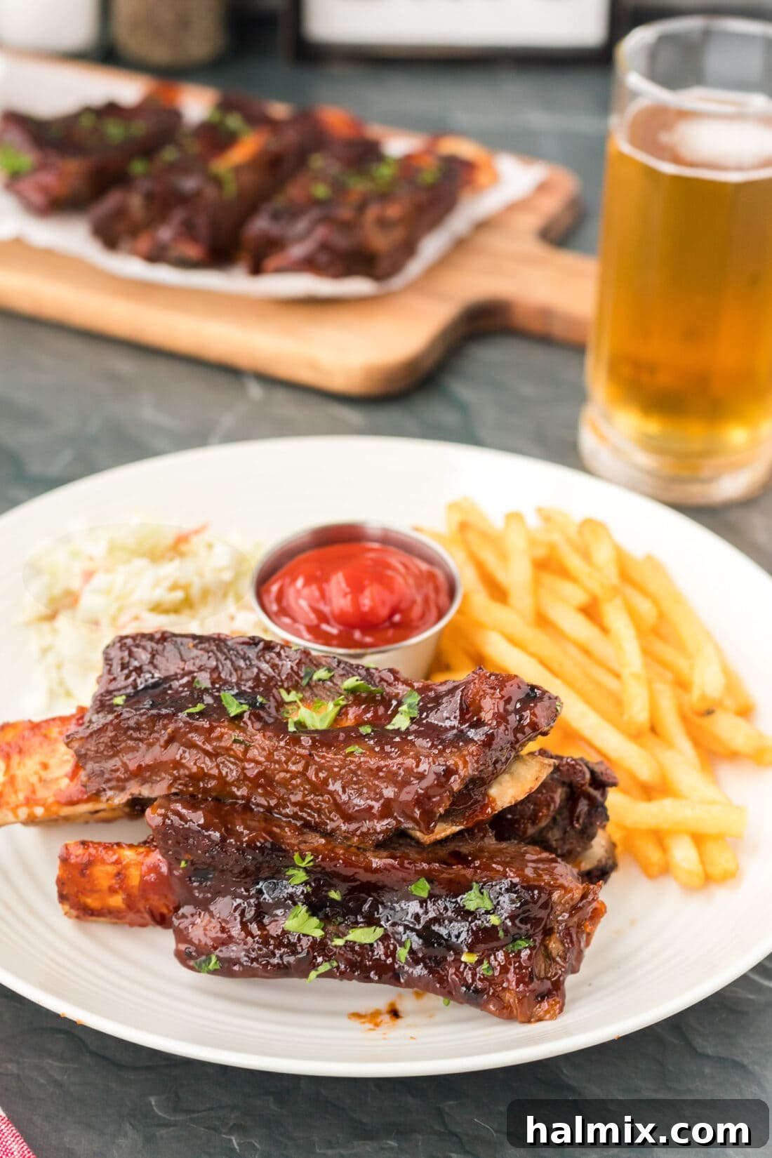 A plate of Instant Pot Beef Ribs served with golden french fries, drizzled with barbecue sauce