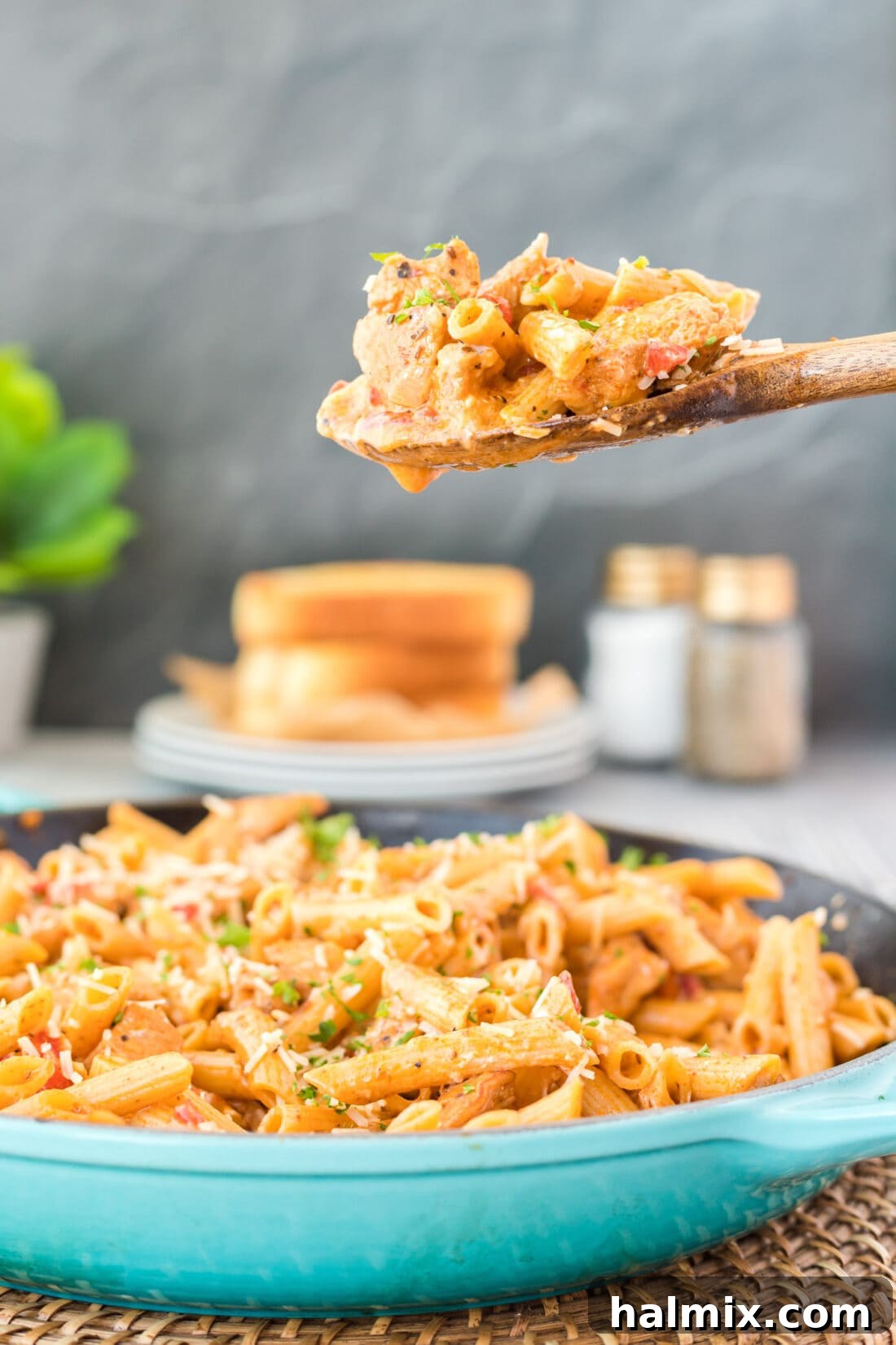 A wooden spoon serving creamy Cajun Chicken Pasta from a skillet, showcasing tender chicken, penne pasta, and roasted bell peppers.