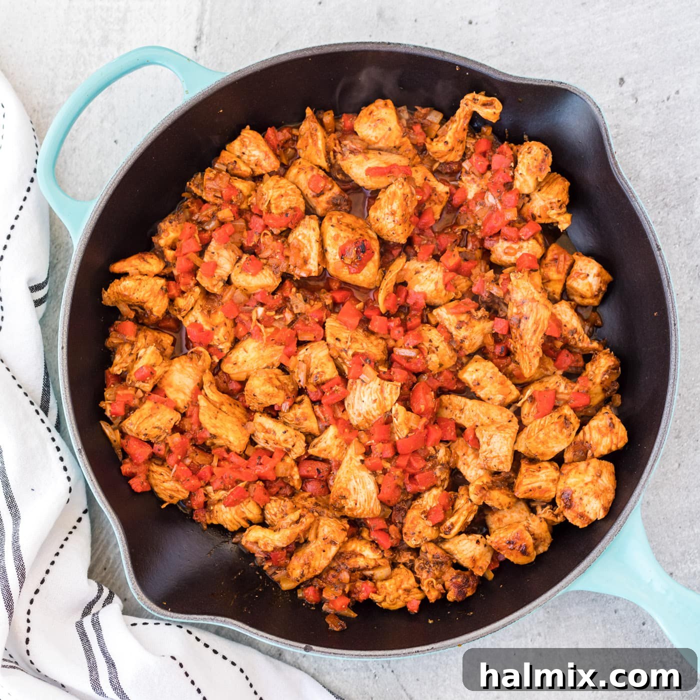Roasted red bell pepper being added to the skillet with cooked Cajun chicken and onions.