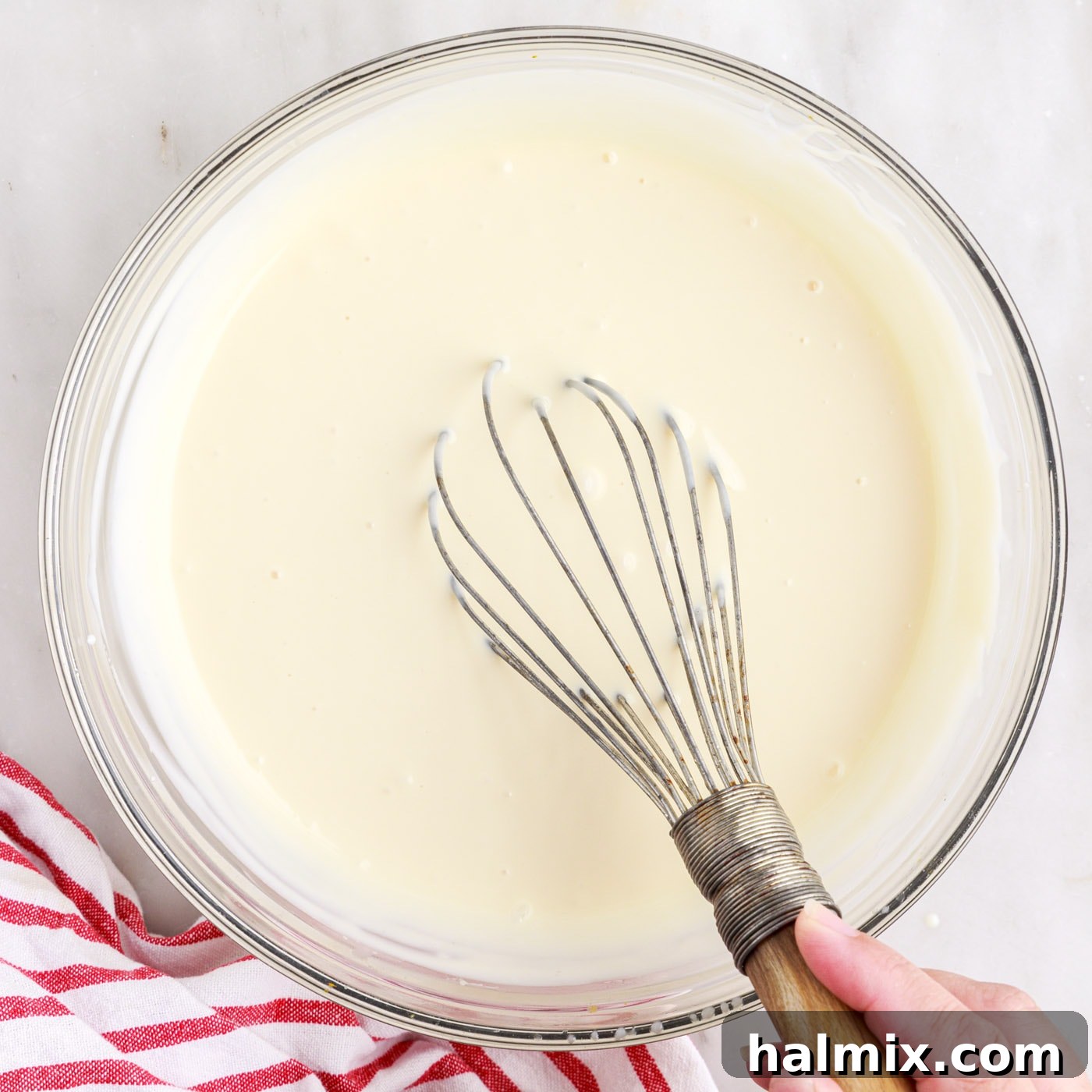 All ingredients for rolled ice cream being whisked together in a large bowl, forming a smooth, creamy base.