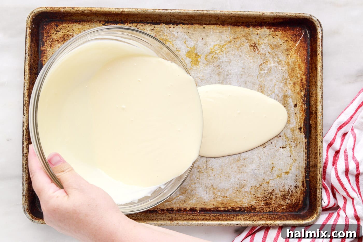 Pouring the liquid rolled ice cream base onto a thoroughly chilled baking sheet, preparing it for spreading.