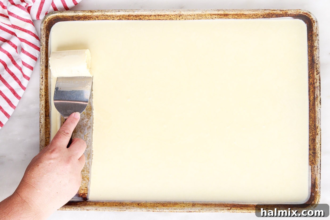 A spatula expertly rolling frozen ice cream mixture off a baking sheet, forming a perfect, delicate roll.