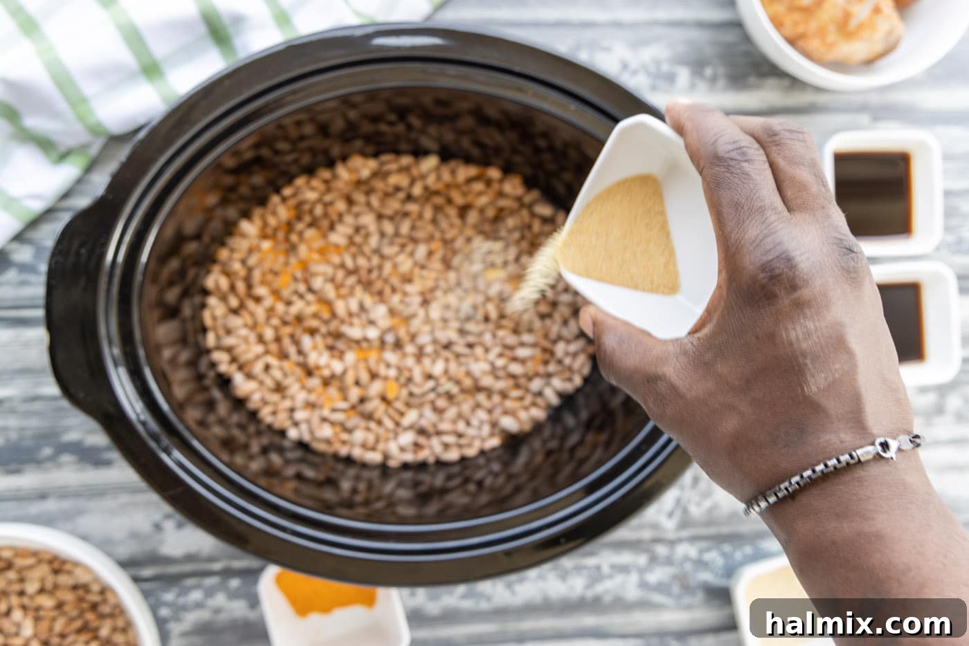 Pouring seasoning over the first layer of pinto beans in a crockpot