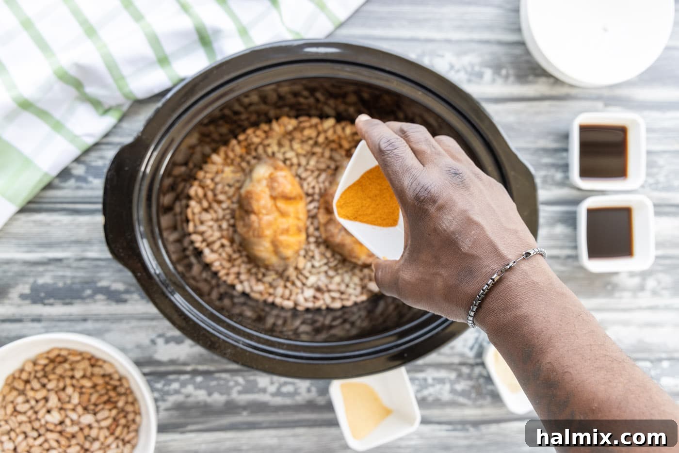Sprinkling additional seasonings over turkey tails and pinto beans in a crockpot