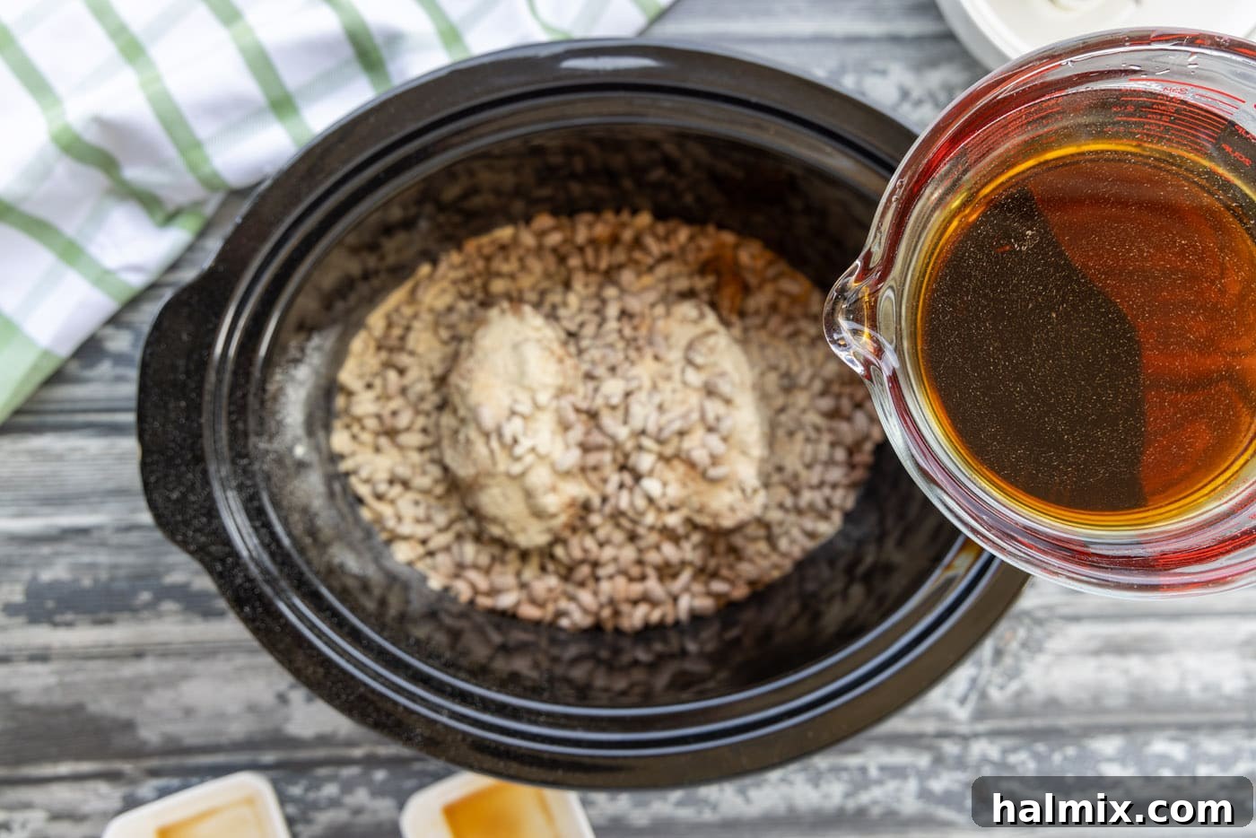 Pouring liquid smoke, soy sauce, and water over pinto beans in the crockpot
