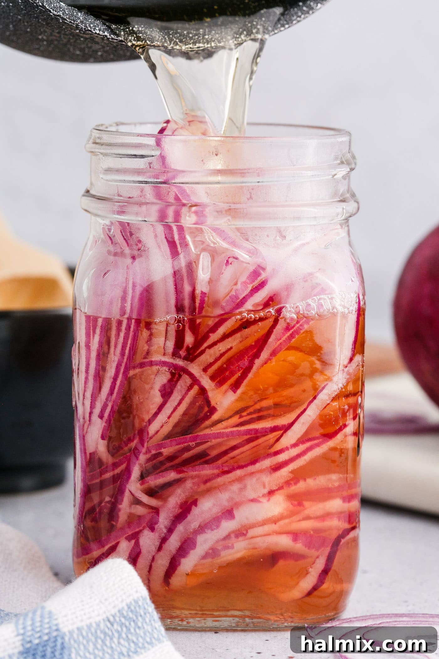 pouring vinegar over sliced red onions in a mason jar