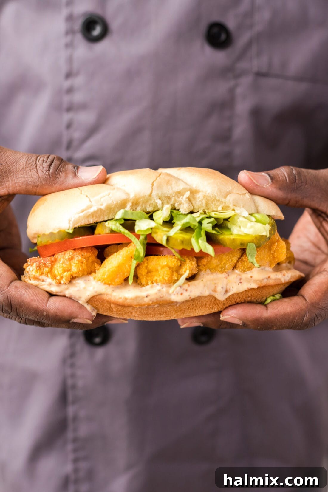 Chef holding a freshly made Shrimp Po Boy sandwich, showcasing its delicious layers and golden-fried shrimp.