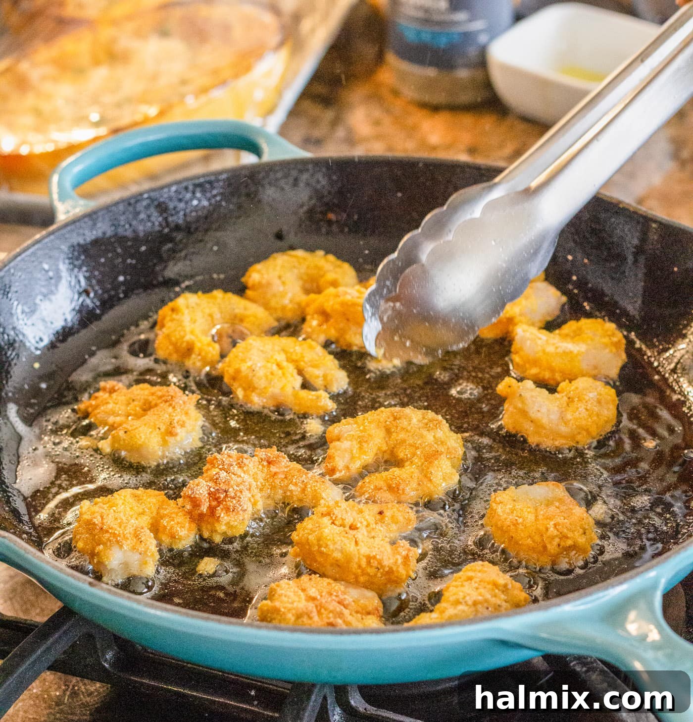 Tongs flipping fried shrimp in a hot skillet, ensuring even cooking and golden-brown perfection.