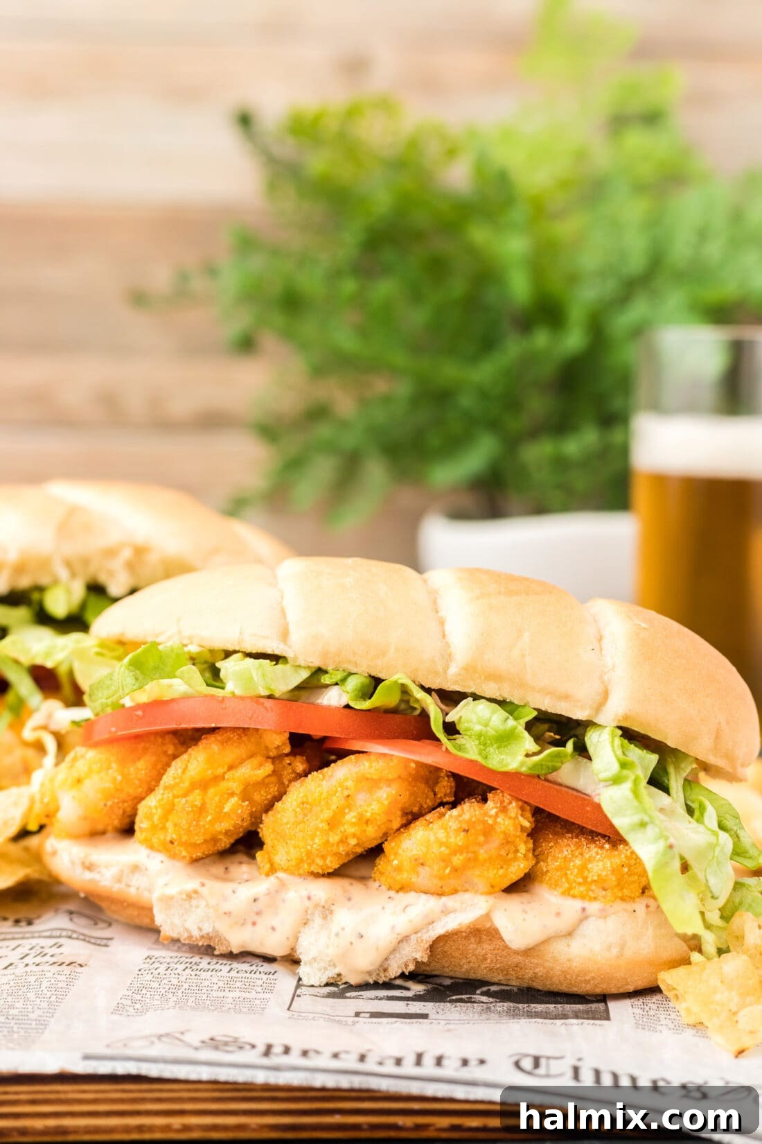 A Shrimp Po Boy sandwich served with a cold beer, highlighting the golden-fried shrimp and fresh toppings.