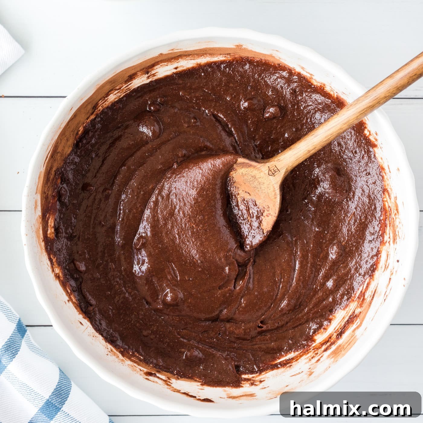 Rich, dark brownie batter in a mixing bowl, stirred with a wooden spoon to a smooth consistency
