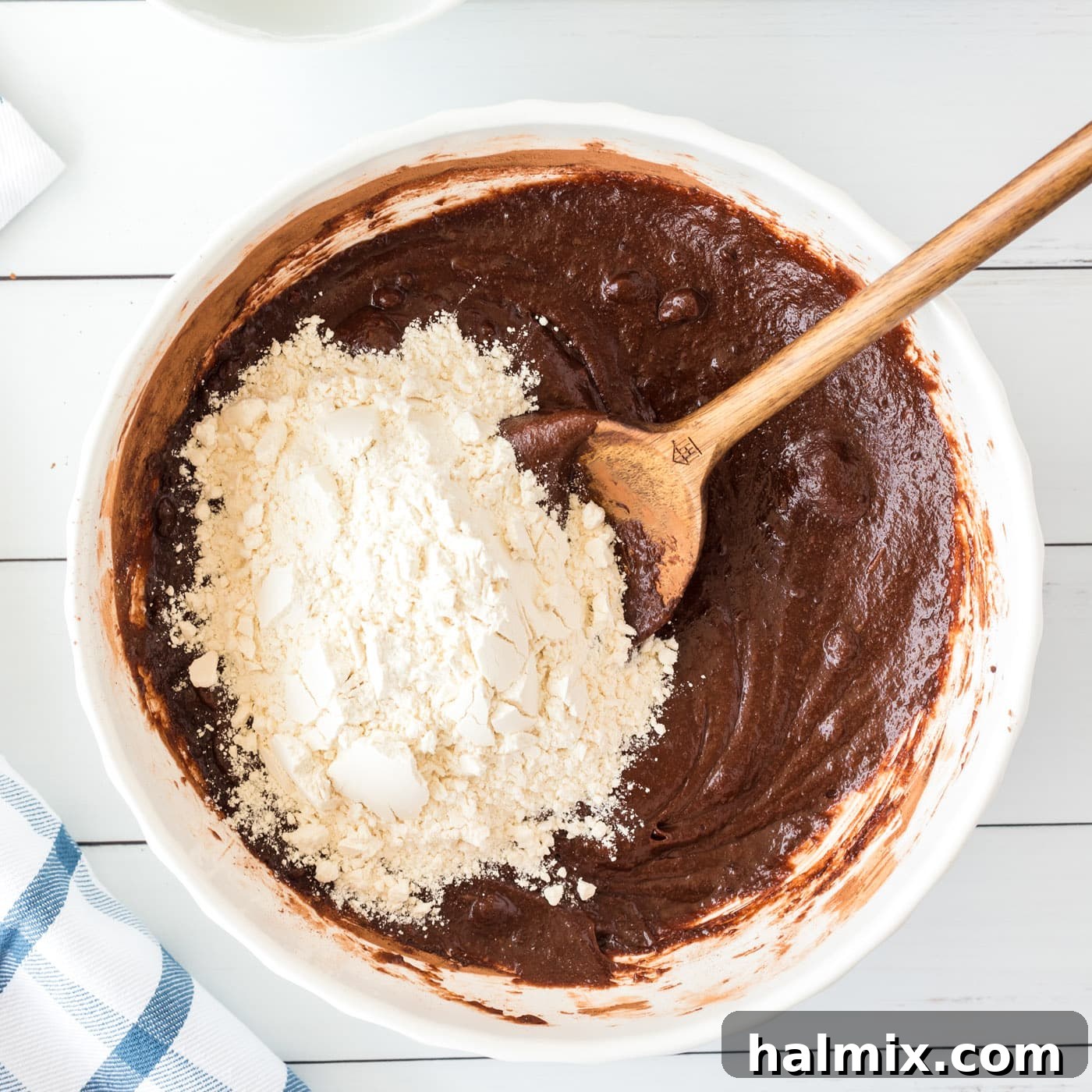 Wooden spoon carefully stirring flour into the brownie batter, ensuring no dry spots remain
