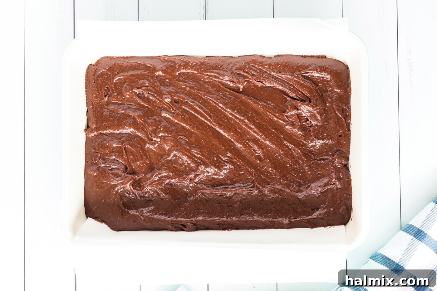 Brownie batter neatly spread in a parchment-lined baking dish, ready for the cookie layer