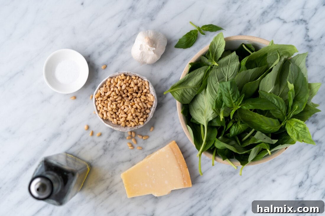 Individual ingredients laid out for making pesto: fresh basil leaves, pine nuts, garlic cloves, Parmesan cheese, and a bottle of extra virgin olive oil.