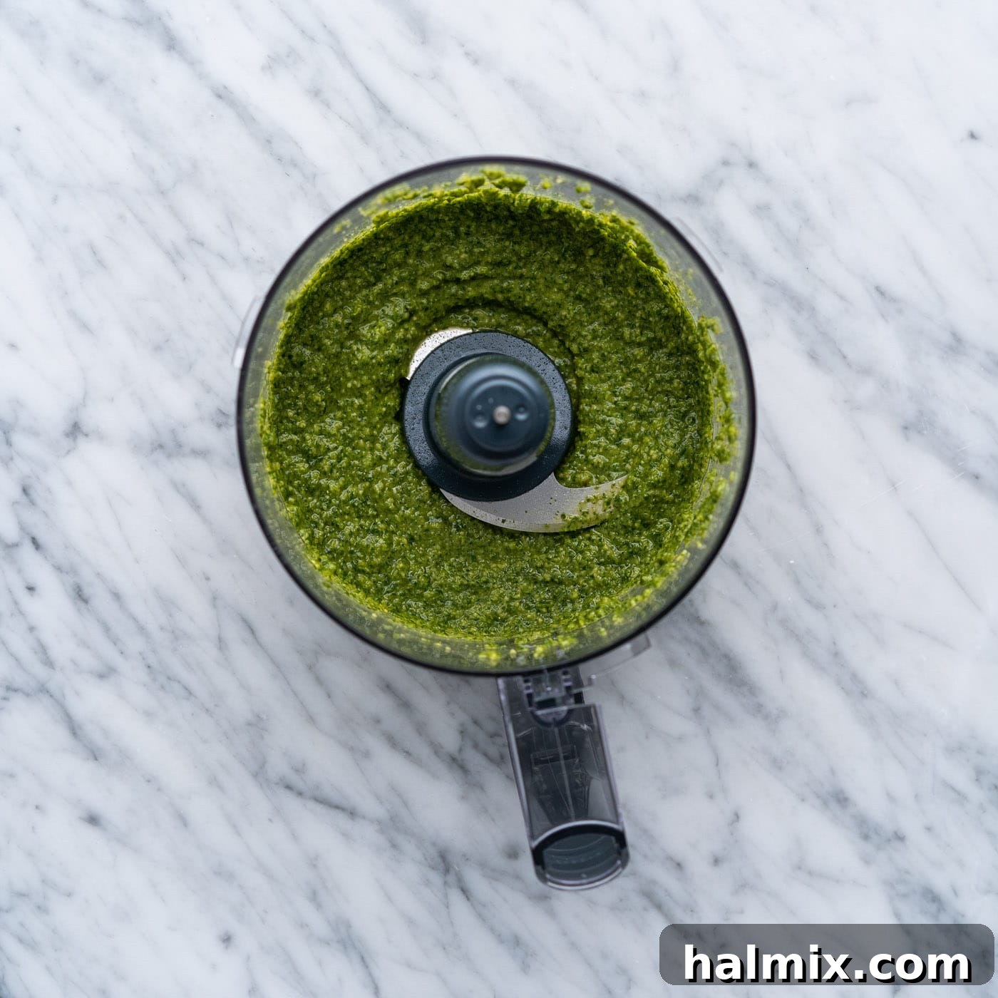 Basil pesto being blended to a smooth consistency in a food processor.