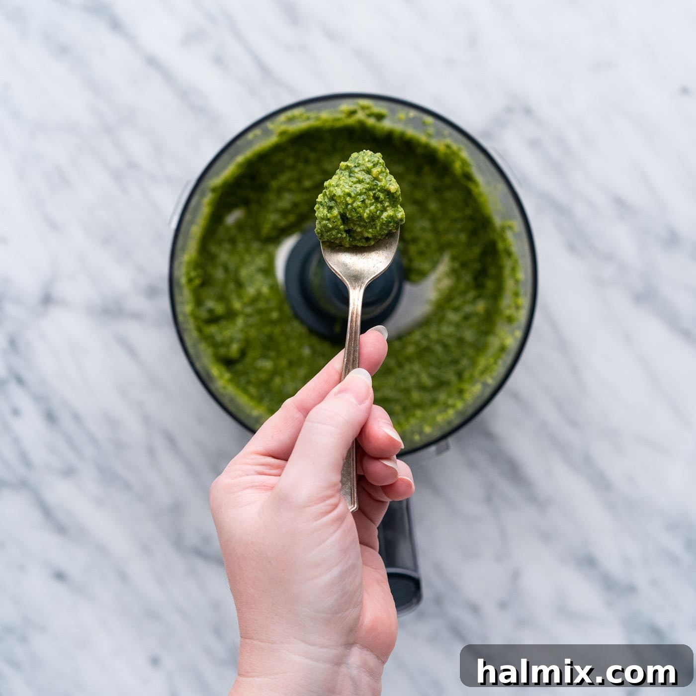 A spoonful of freshly made basil pesto lifted from the food processor, showing its rich green color and smooth texture.