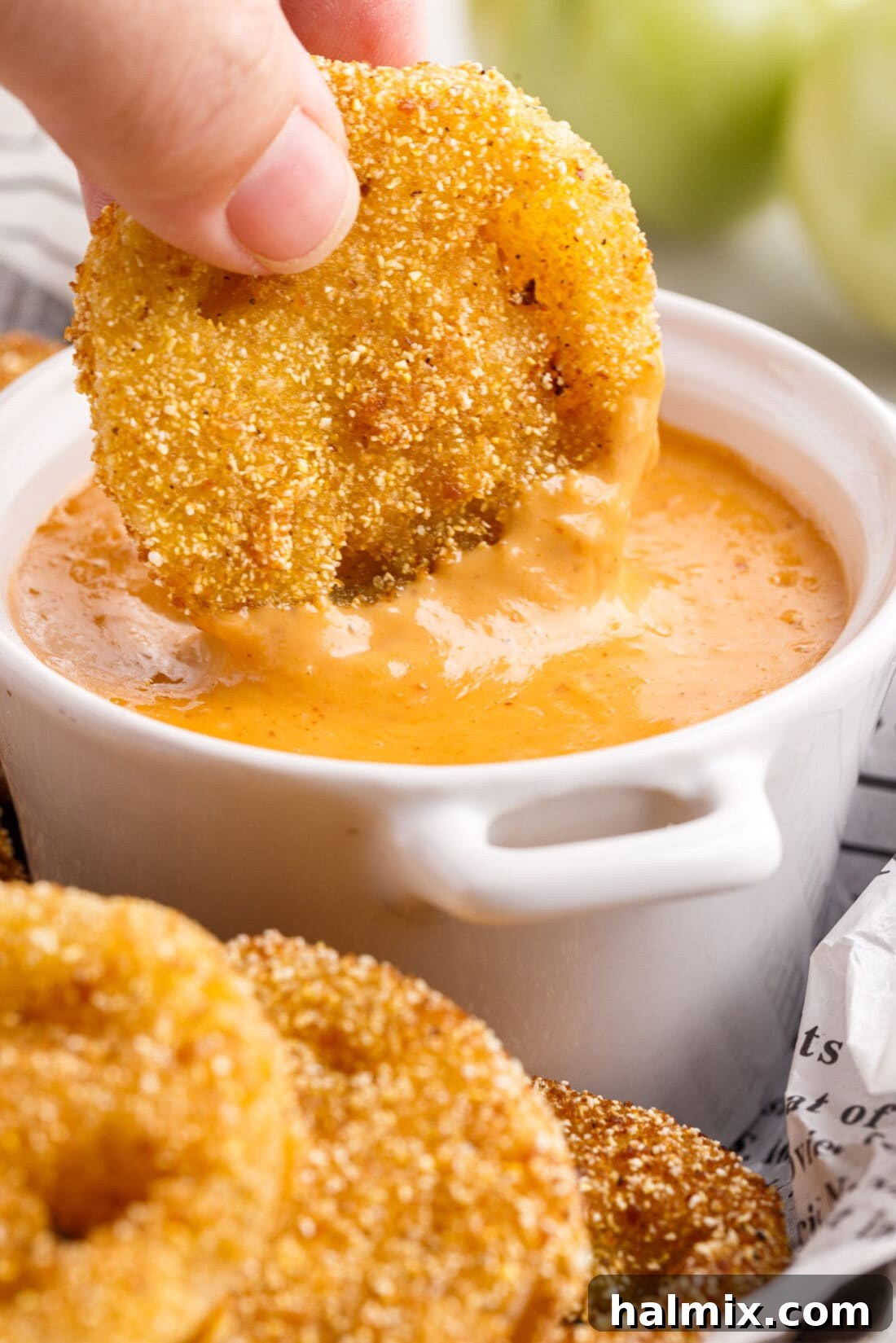 Crispy Fried Green Tomato being dipped into a creamy sauce, showcasing its golden crust and tender interior