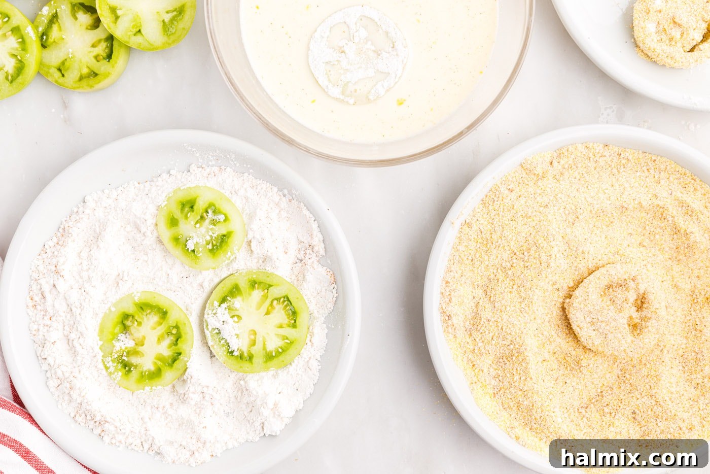 A green tomato slice being carefully coated in a sequence of flour, egg, and breadcrumb mixtures