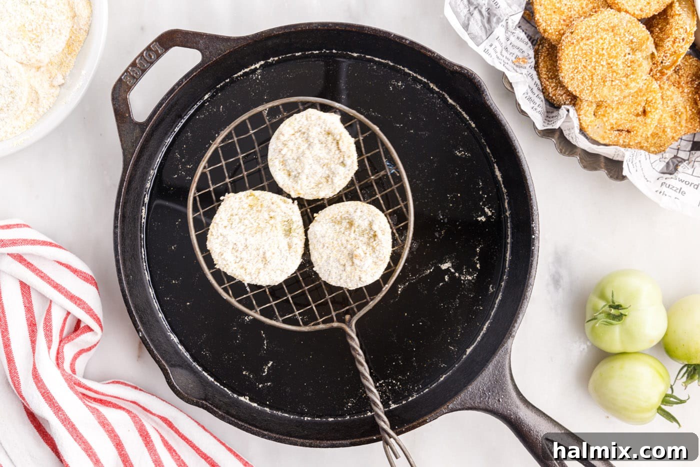 Dredged green tomatoes being gently lowered into hot oil for frying