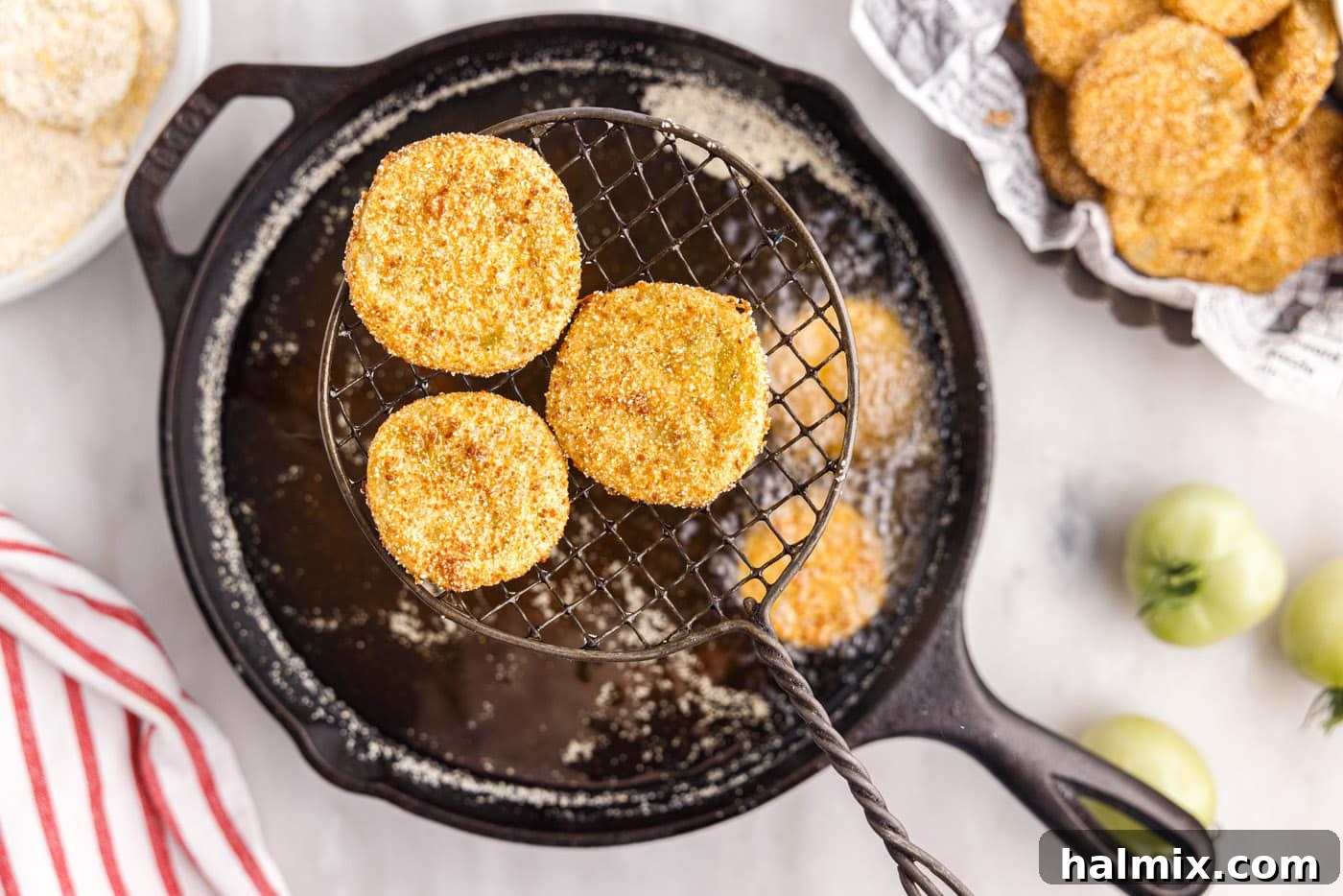 Freshly fried green tomatoes being lifted from hot oil with a slotted spoon to drain