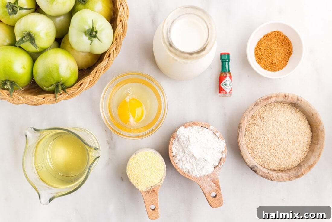 A collection of ingredients laid out on a table: green tomatoes, flour, breadcrumbs, cornmeal, milk, eggs, and seasonings for making fried green tomatoes