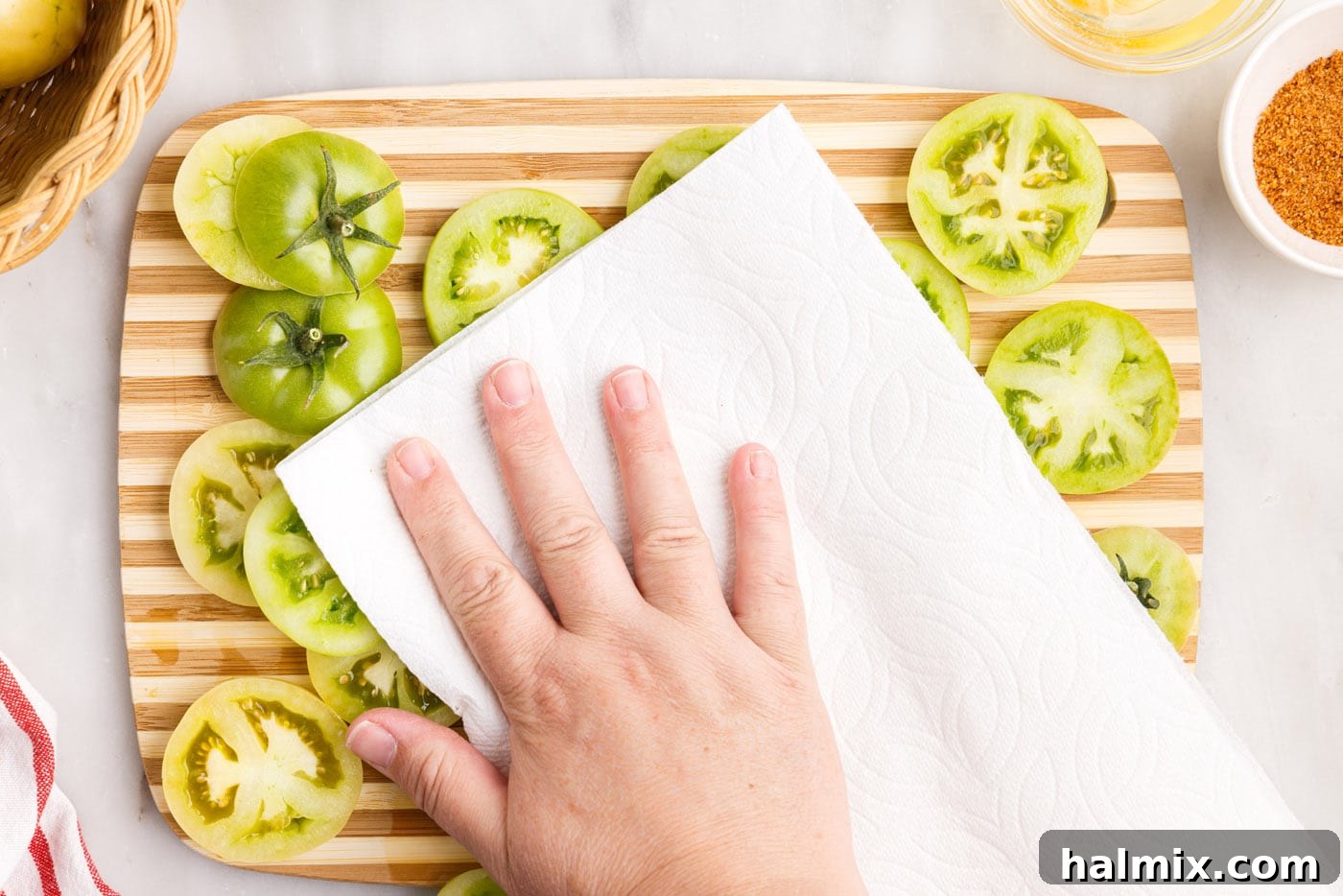 Paper towels gently patting down sliced green tomatoes to absorb excess moisture