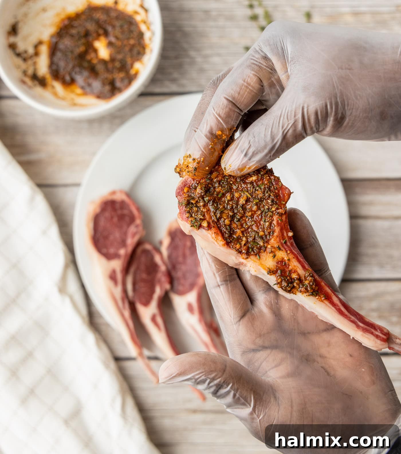 Gloved hands carefully rubbing spices onto raw lamb loin chops