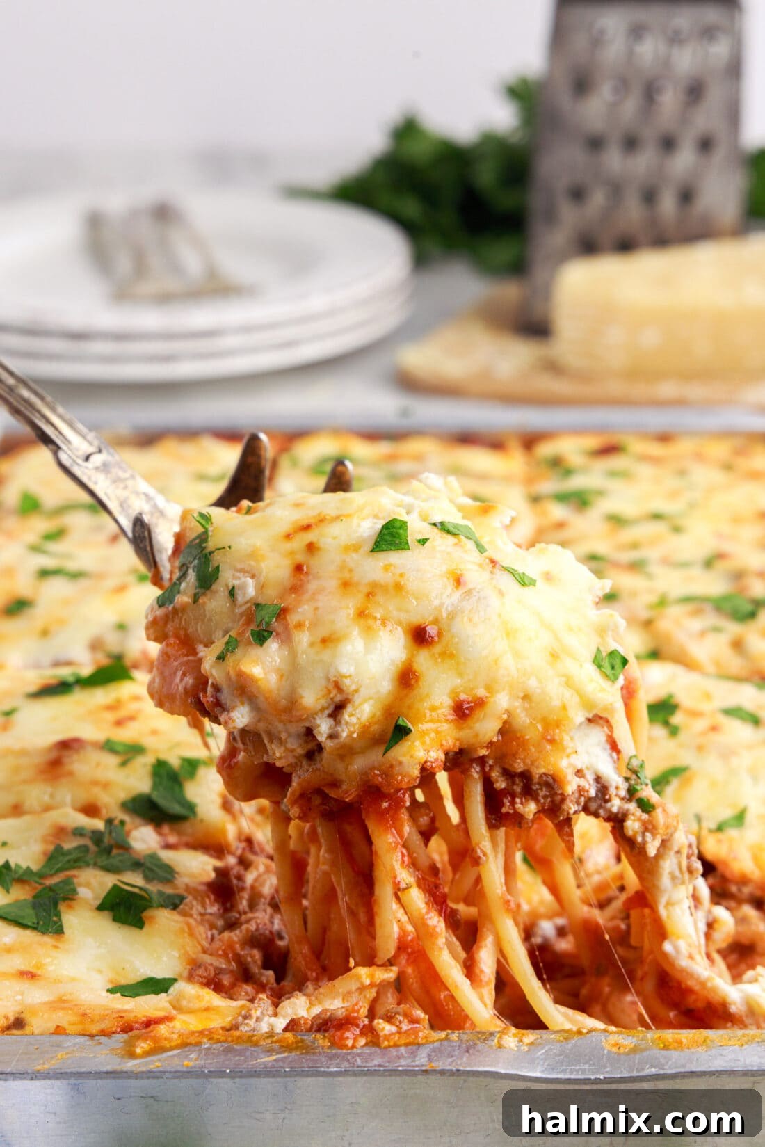 A serving of Million Dollar Spaghetti being lifted from a casserole dish, showing the layers of pasta, meat sauce, and melted cheese.