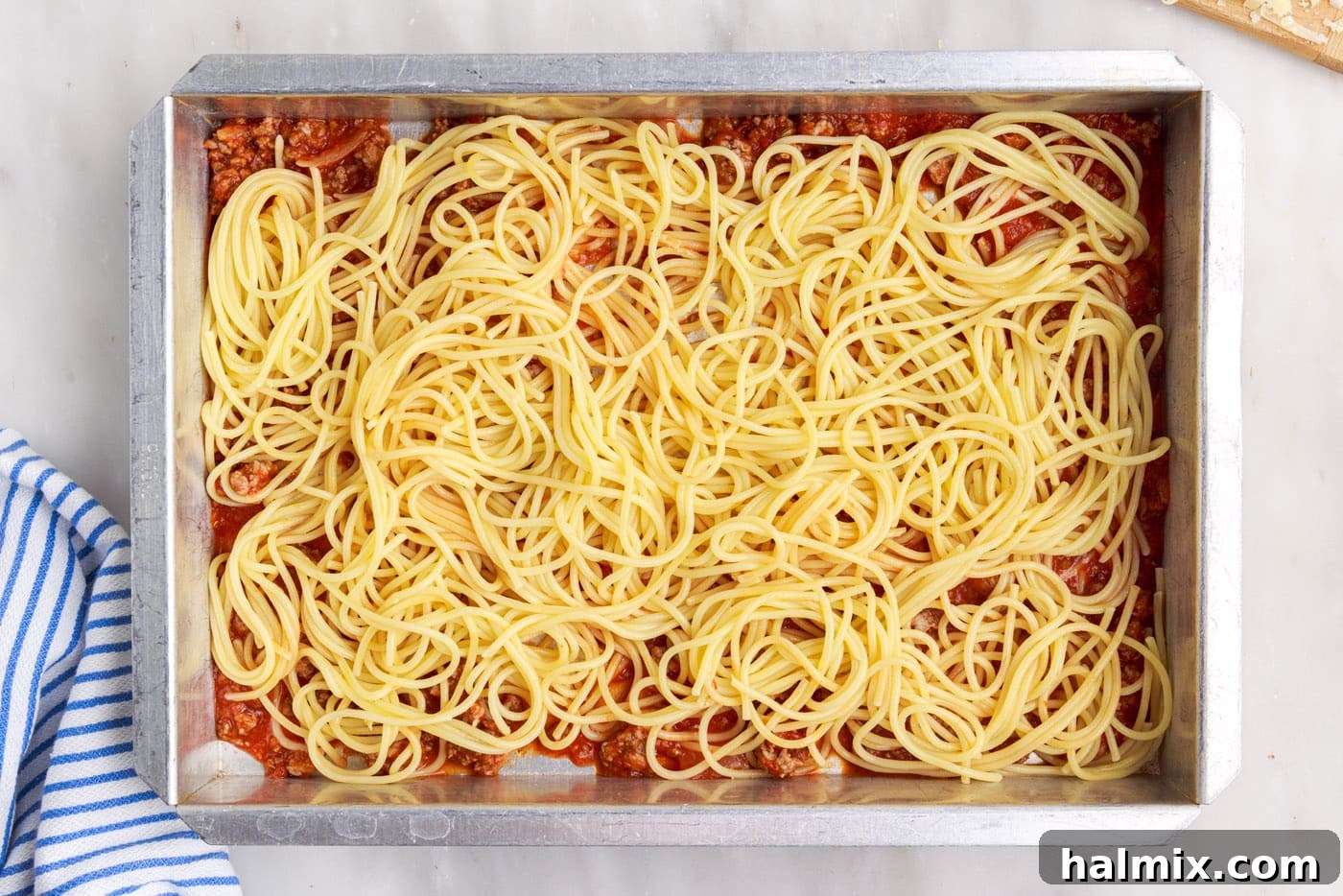 Cooked spaghetti noodles carefully laid over the meat sauce in a baking pan, forming the first pasta layer.