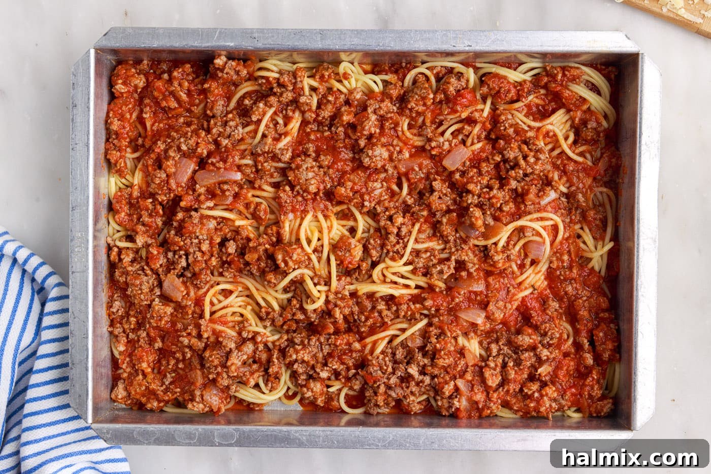 Another layer of savory meat sauce spread over the spaghetti in the baking dish, continuing the layering process.