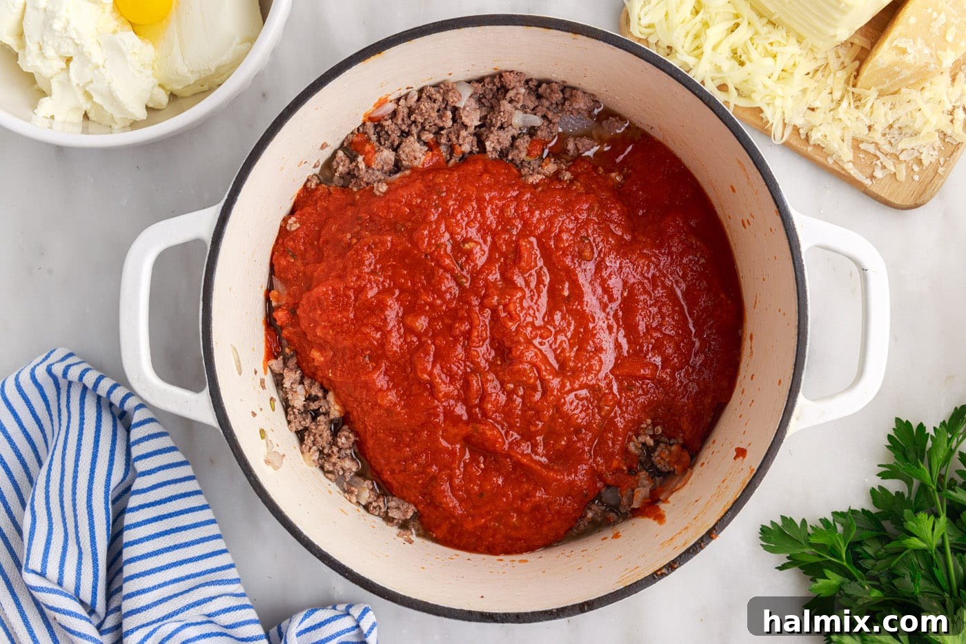 Marinara sauce being stirred into a skillet with cooked ground meat and onions, creating a rich meat sauce.