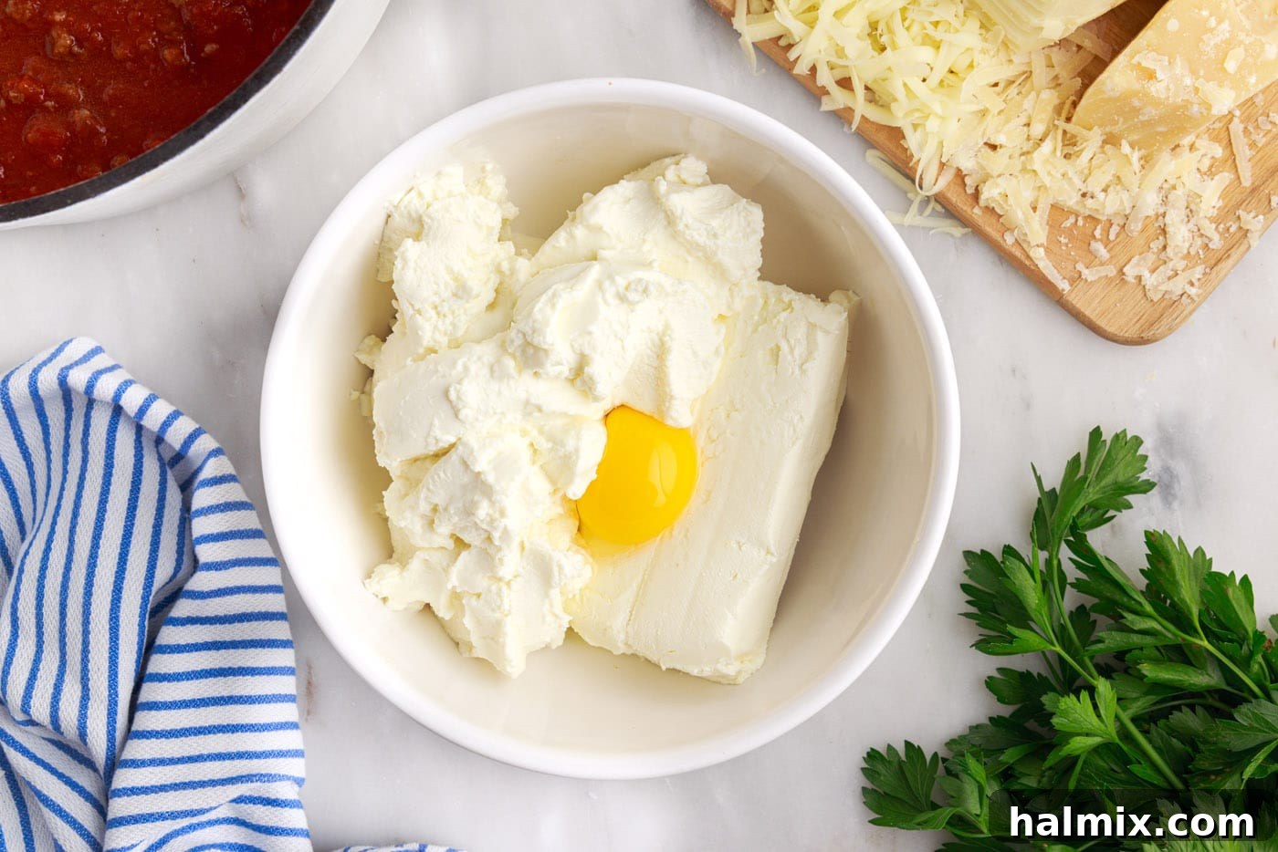 Ricotta cheese, cream cheese, and an egg in a mixing bowl, ready to be beaten.