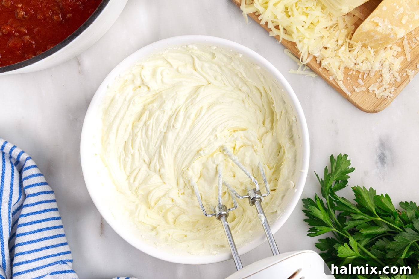 A hand mixer blending ricotta, cream cheese, and egg in a bowl until smooth and creamy.