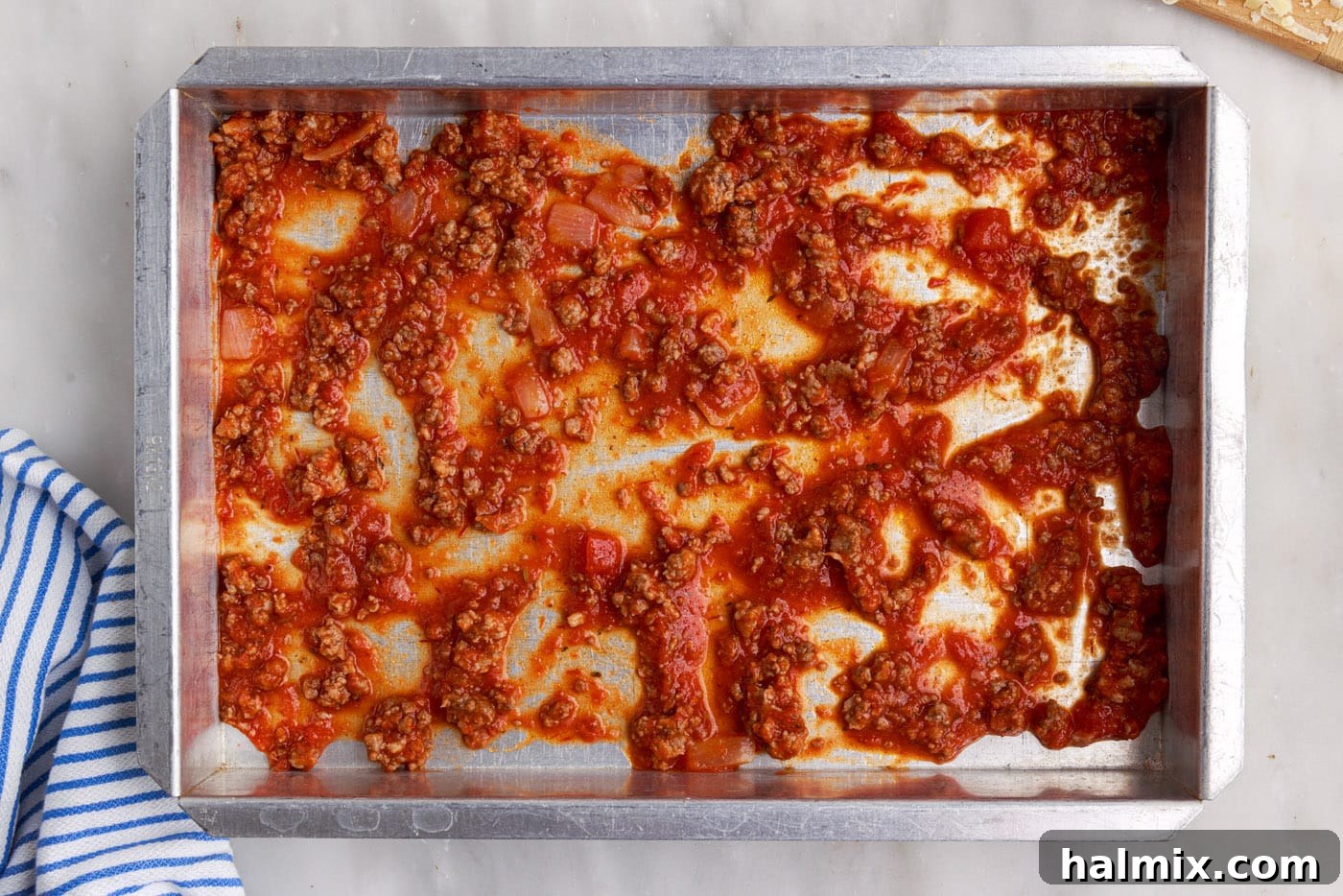 A layer of rich meat sauce spread evenly at the bottom of a 9x13 inch baking pan, ready for the next layer.