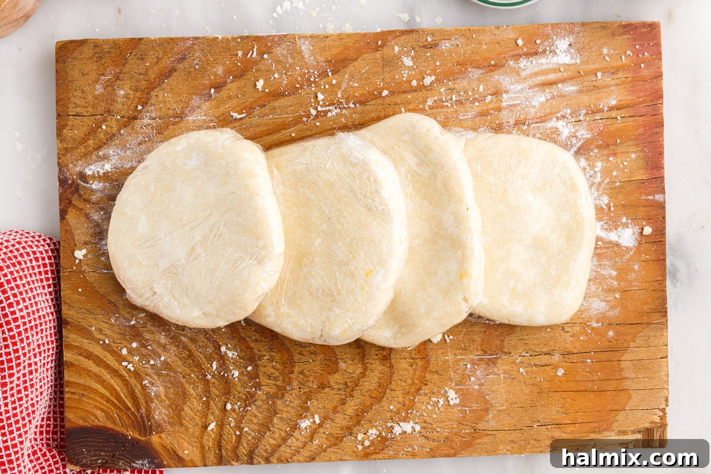 Four flattened rugelach dough discs, individually wrapped in plastic, ready for refrigeration.