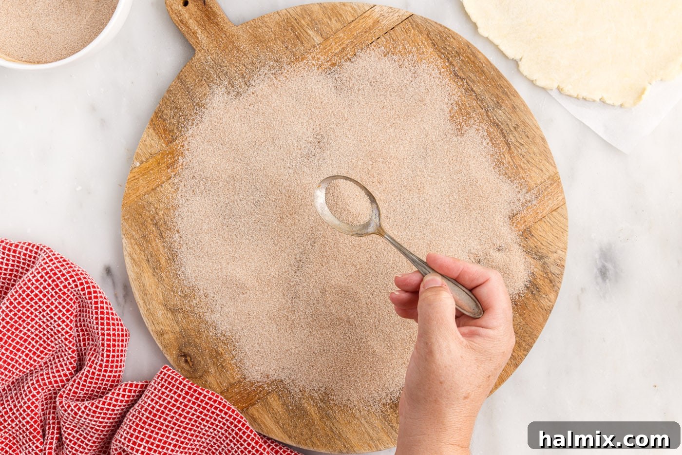 Cinnamon sugar is sprinkled generously over a cutting board, preparing the surface for the dough.