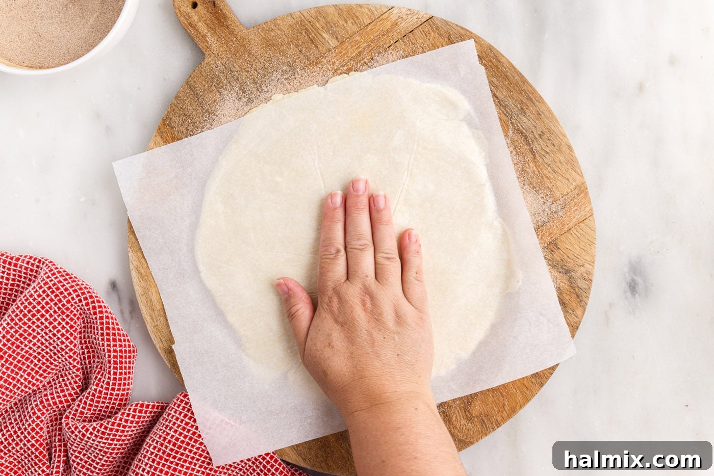 A hand gently presses down on the rugelach dough disc, ensuring the cinnamon sugar adheres to the bottom surface.